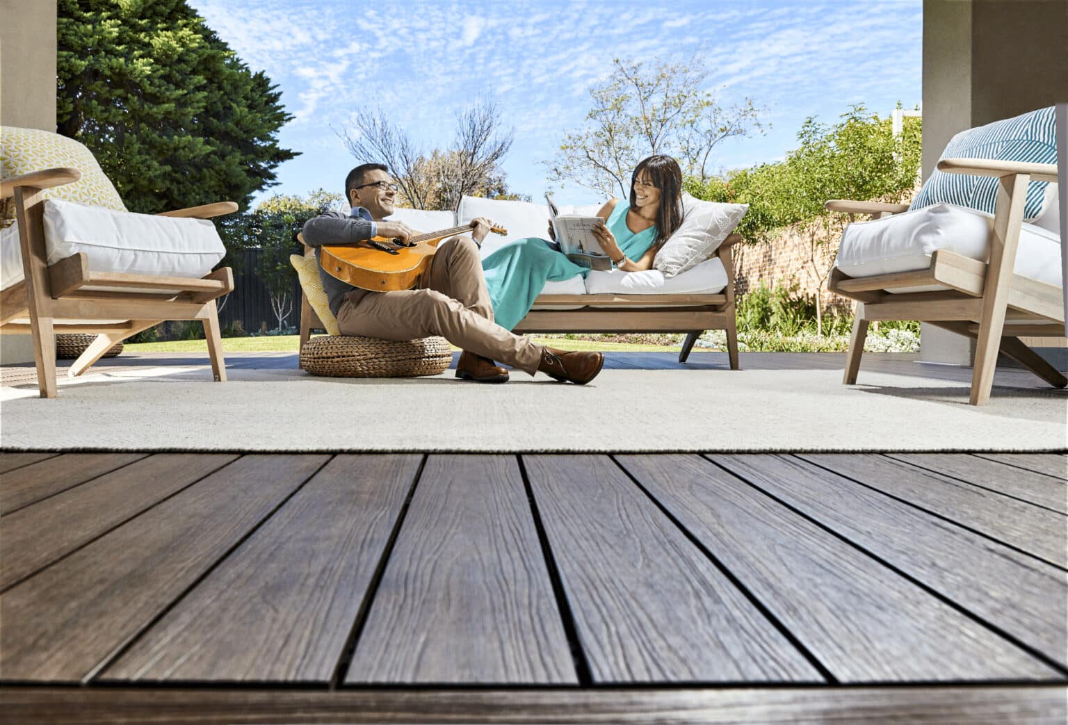 a man playing a guitar whilst his wife reads a book on their deck