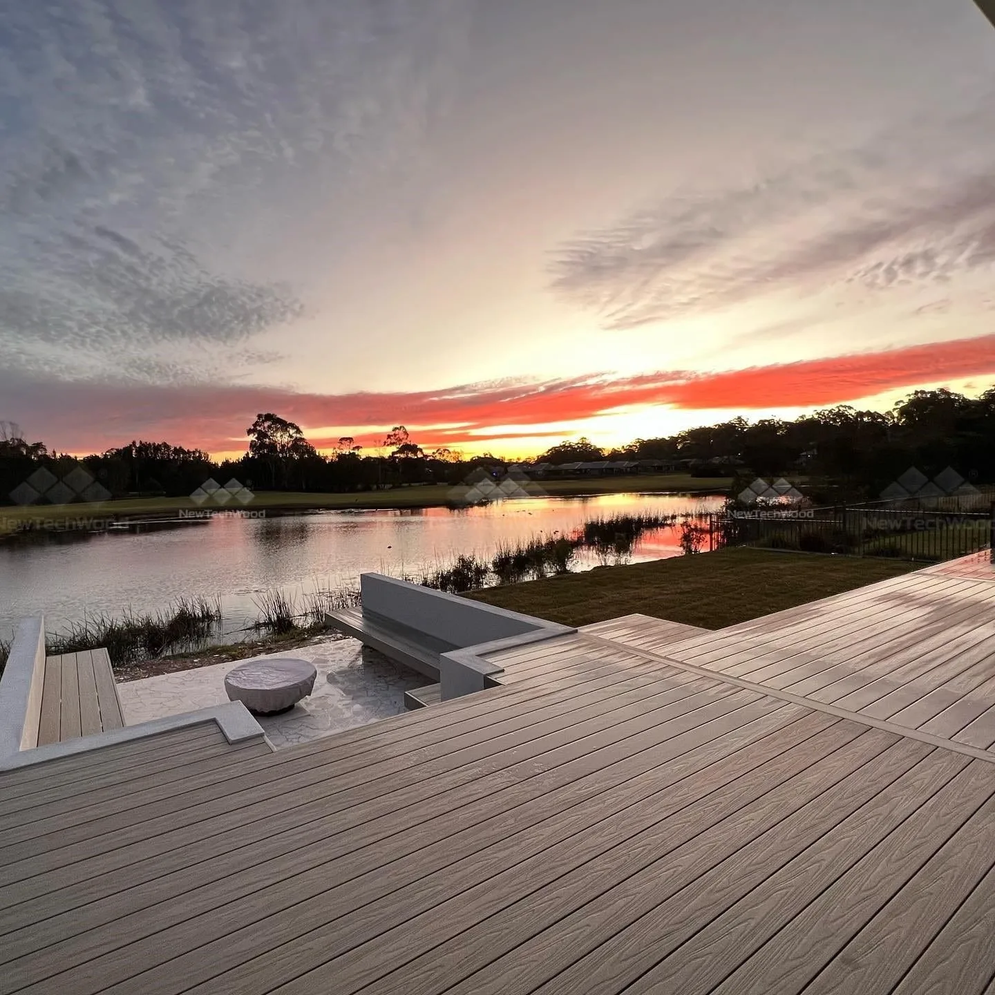 A spacious outdoor deck with a lake view at sunset, featuring a built-in seating area.