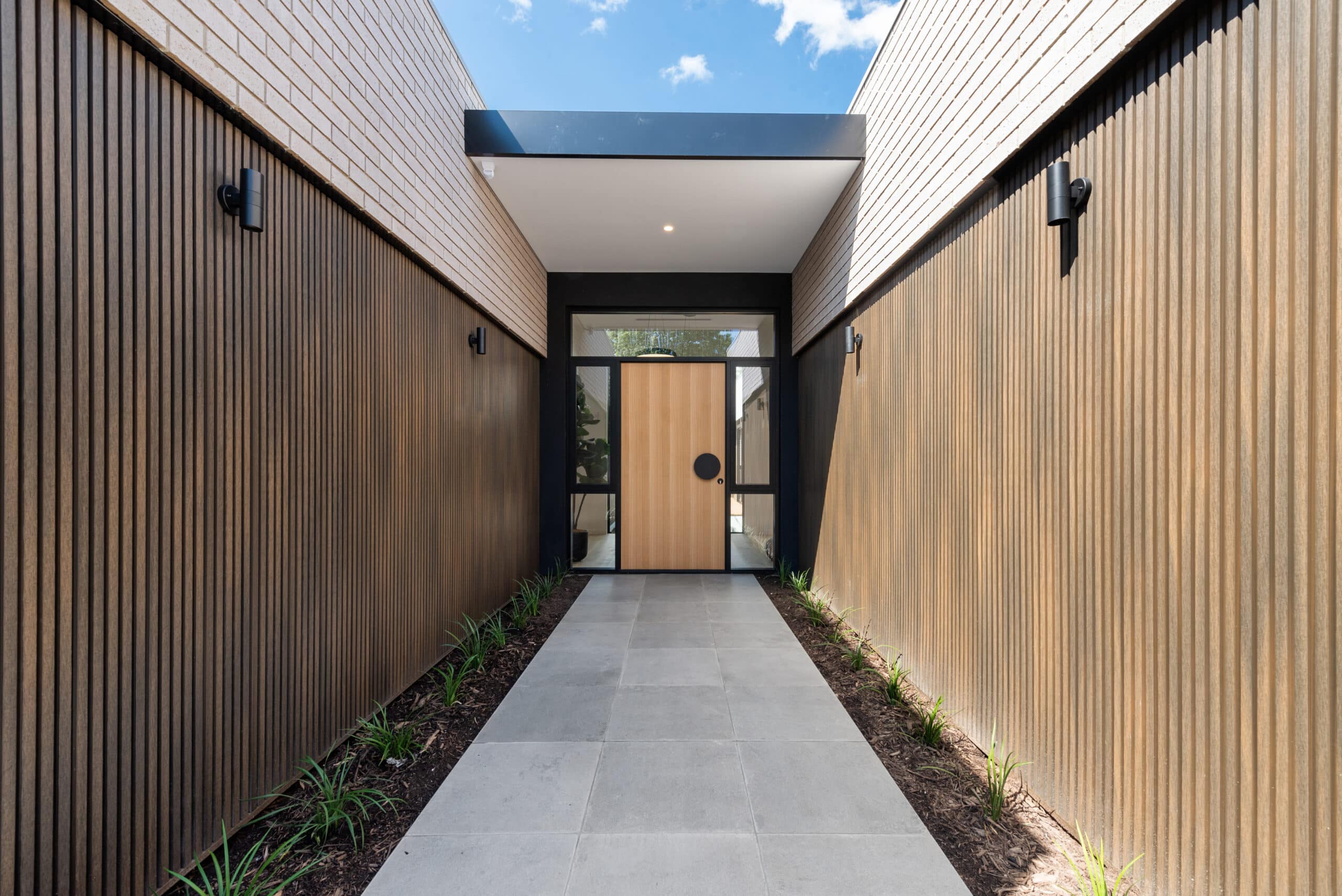 A modern entryway with vertical wooden slat walls, a sleek pathway, and a stylish wooden front door.