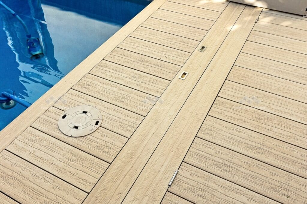 Detailed view of light wooden composite deck with built-in flush deck lights and a pool maintenance hatch.