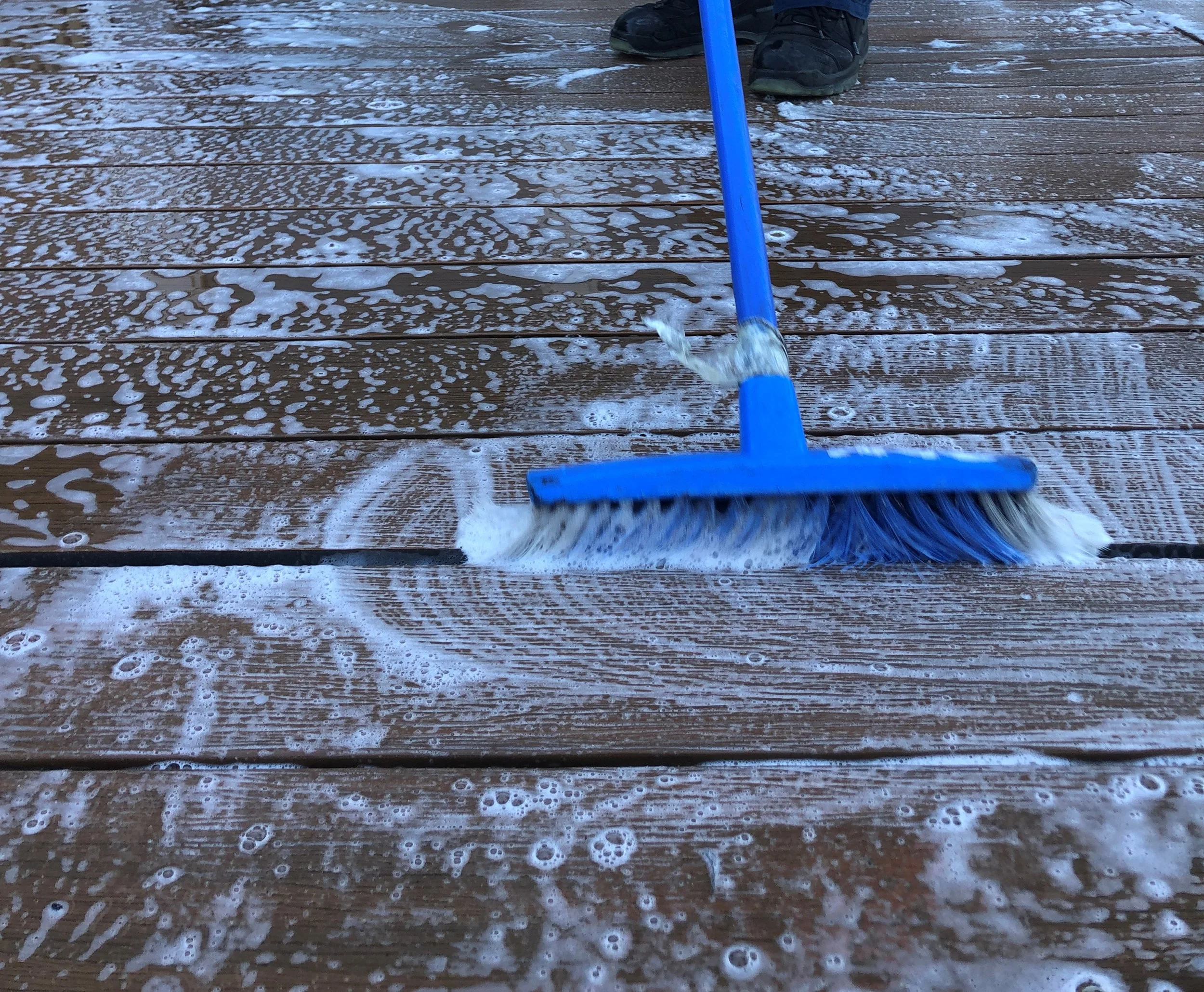 Thorough cleaning of a wooden deck using a blue broom and DECKWash, showcasing effective maintenance techniques for outdoor spaces.