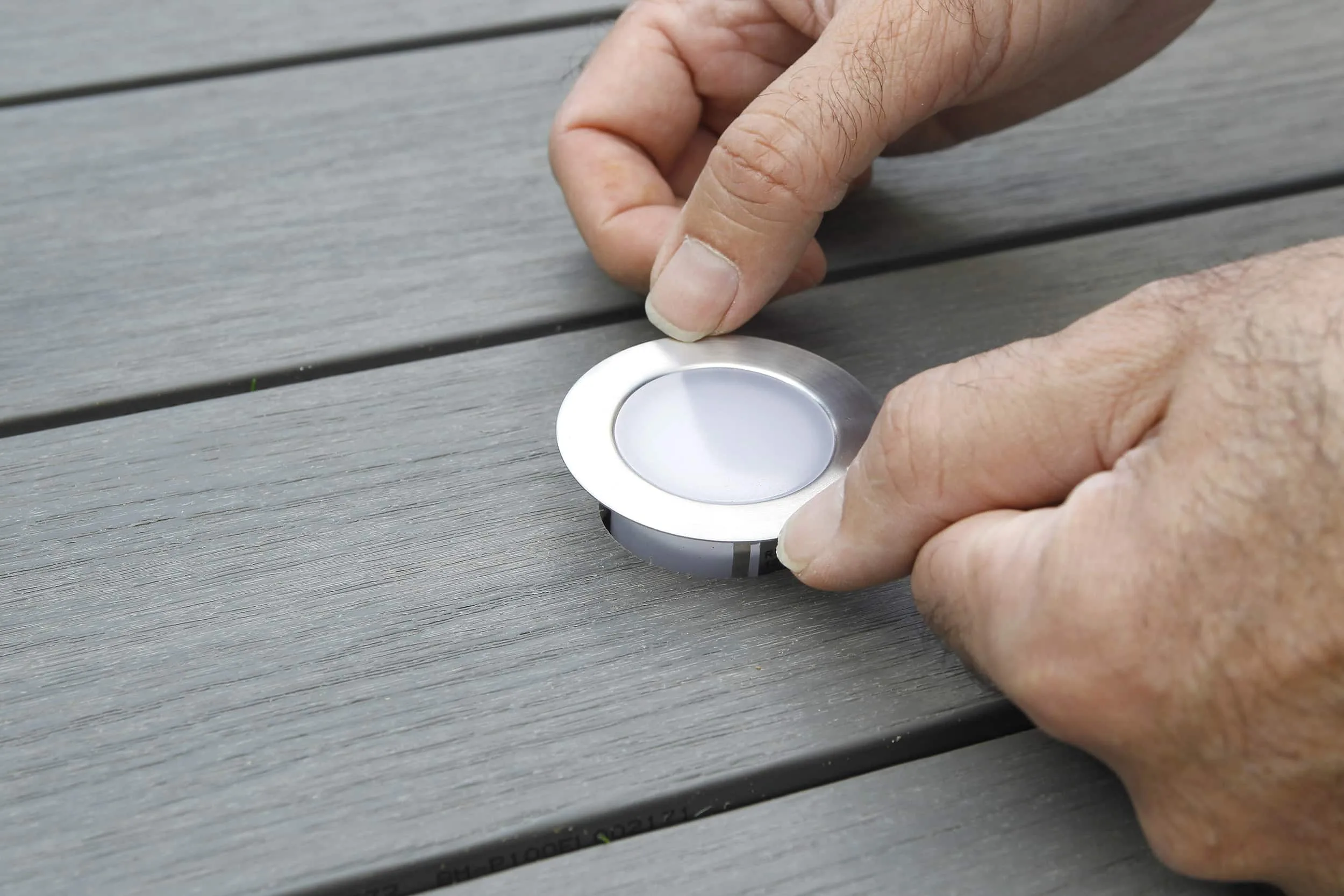 Hand installing a modern OWLIA LED deck light into composite decking, enhancing outdoor ambiance and safety.