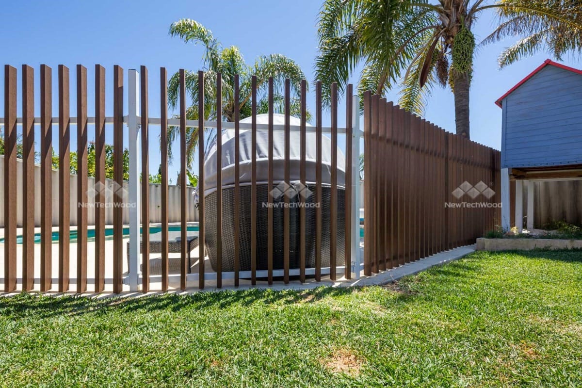 Outdoor area with a pool surrounded by vertical wooden slat fencing, palm trees, and a partially visible blue shed in the background