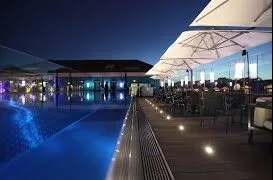 Luxurious rooftop poolside deck illuminated by elegant OWLIA decking lights, enhancing a night time social venue atmosphere