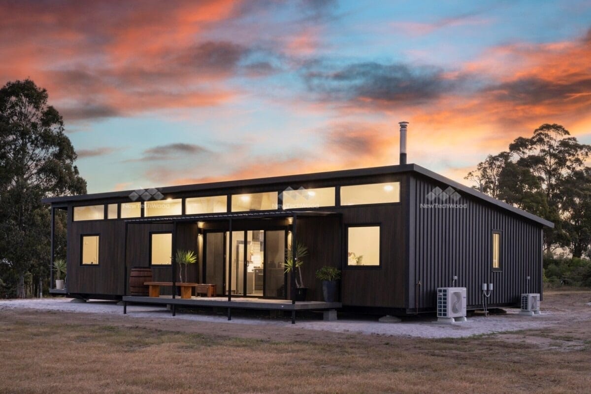 Modern modular home with expansive decking at dusk, featuring a striking sunset backdrop and minimalist design