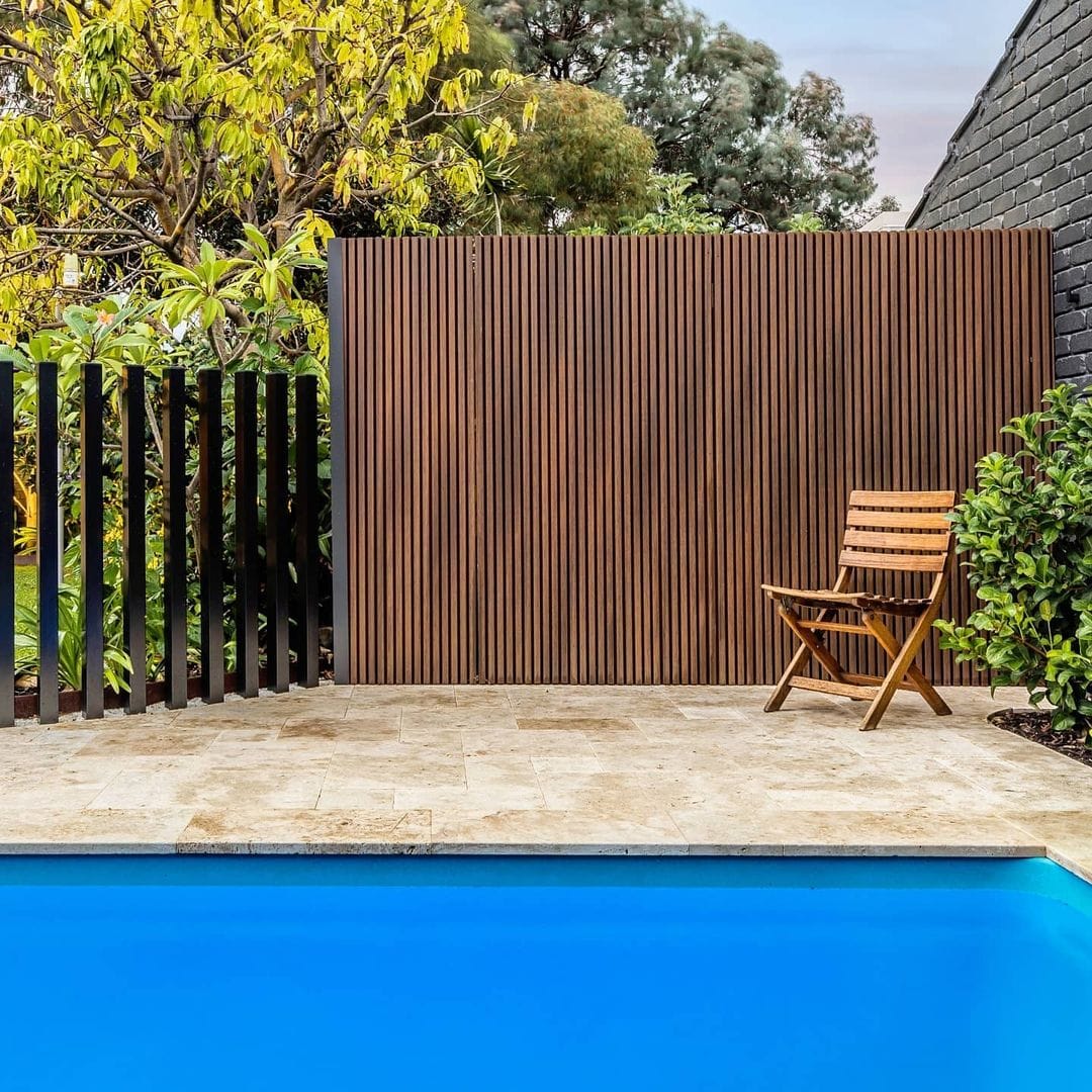 Tranquil backyard setting with vertical wooden panel fencing, a folding chair, and vibrant poolside flora.
