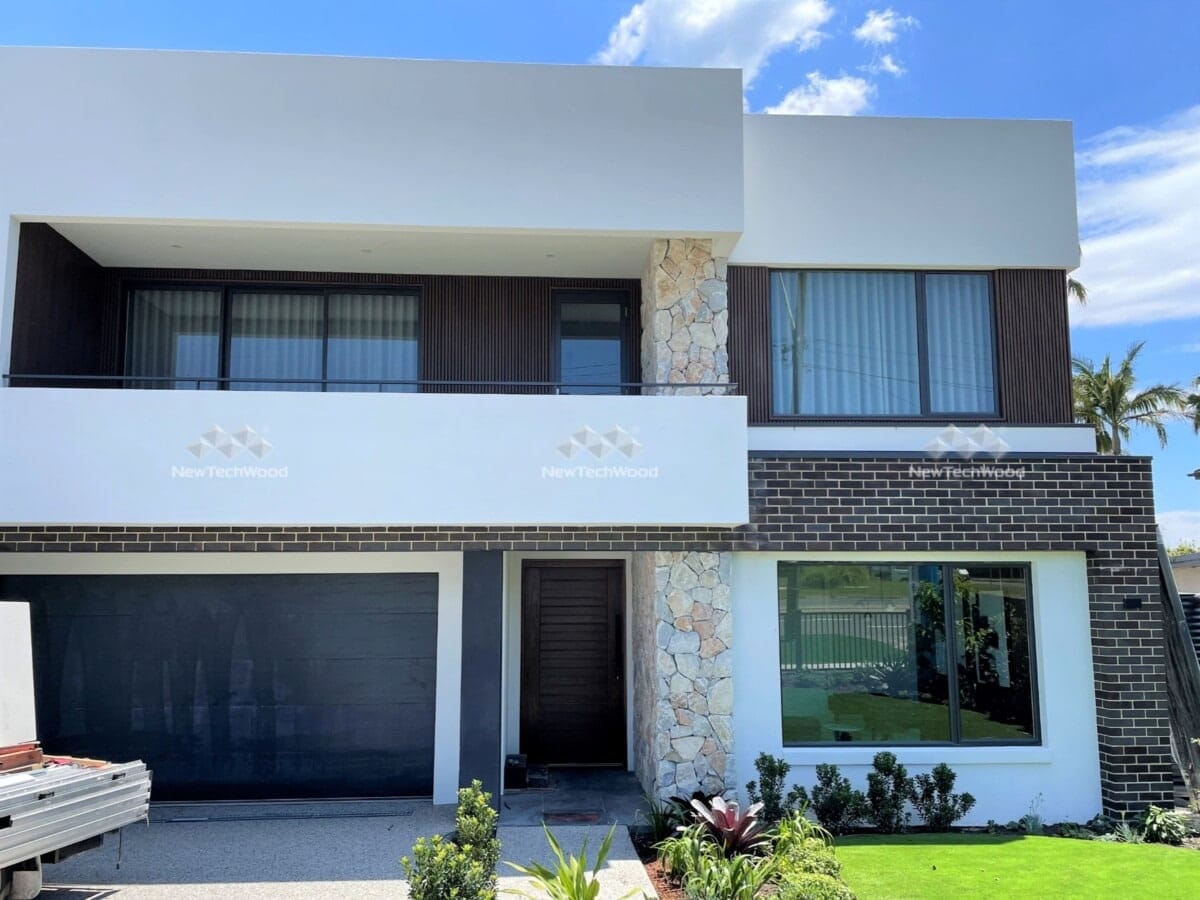 Modern two-story home featuring upstairs composite cladding, stone accents, and a sleek garage door.