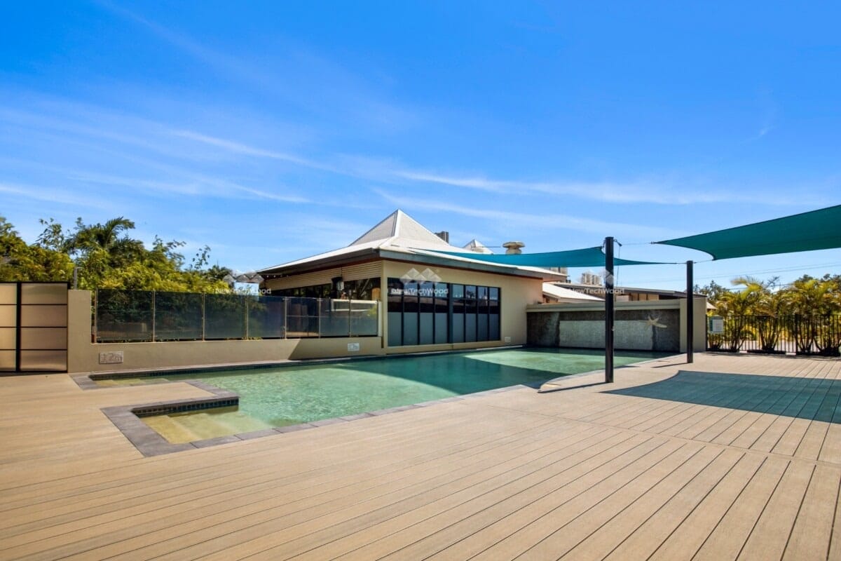 Expansive outdoor pool deck with modern decking, integrated into a residential setting with clear pool fences and a shaded lounge area