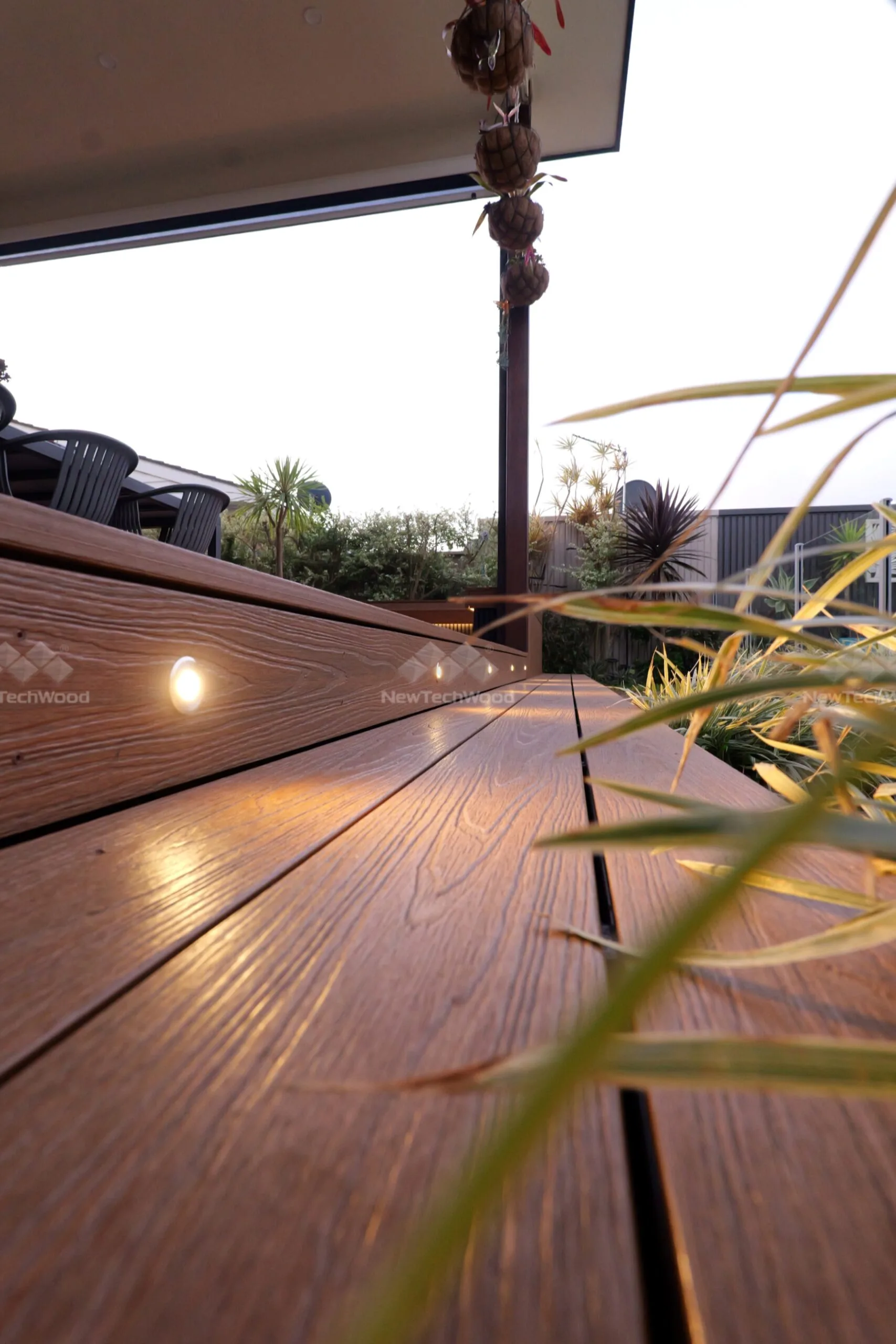 A detailed view of NewTechWood composite decking with a rich wood texture, enhanced by warm lighting and modern landscaping.