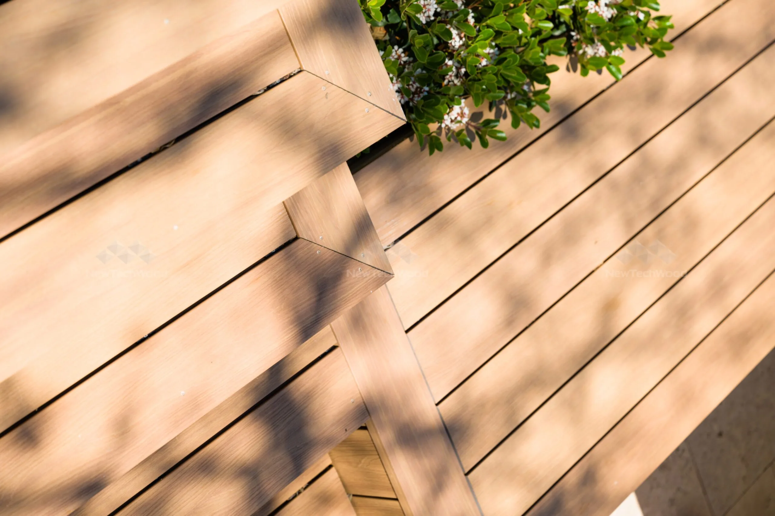 NewTechWood composite decking showcasing realistic timber grain and texture. A close-up of precisely cut and installed composite decking, showcasing a seamless mitered corner design with warm natural wood tones and secure stainless steel fasteners.