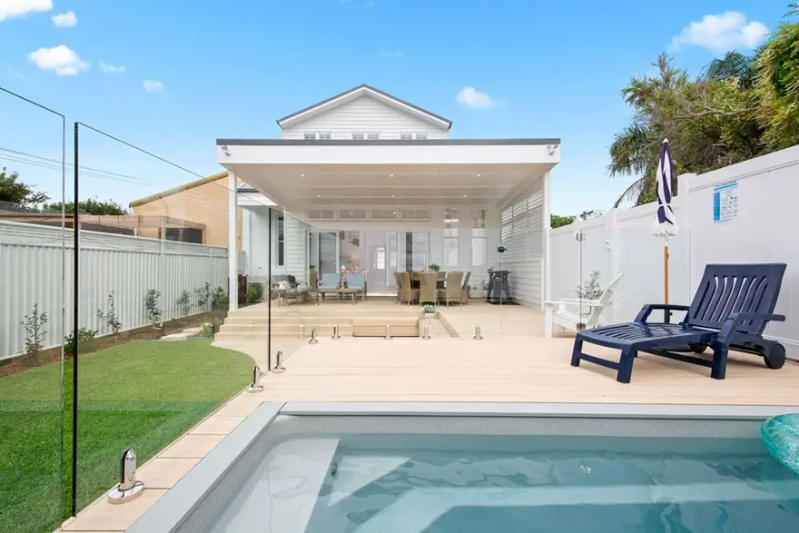 A contemporary home with a covered outdoor dining area, glass pool fencing, and light composite decking.