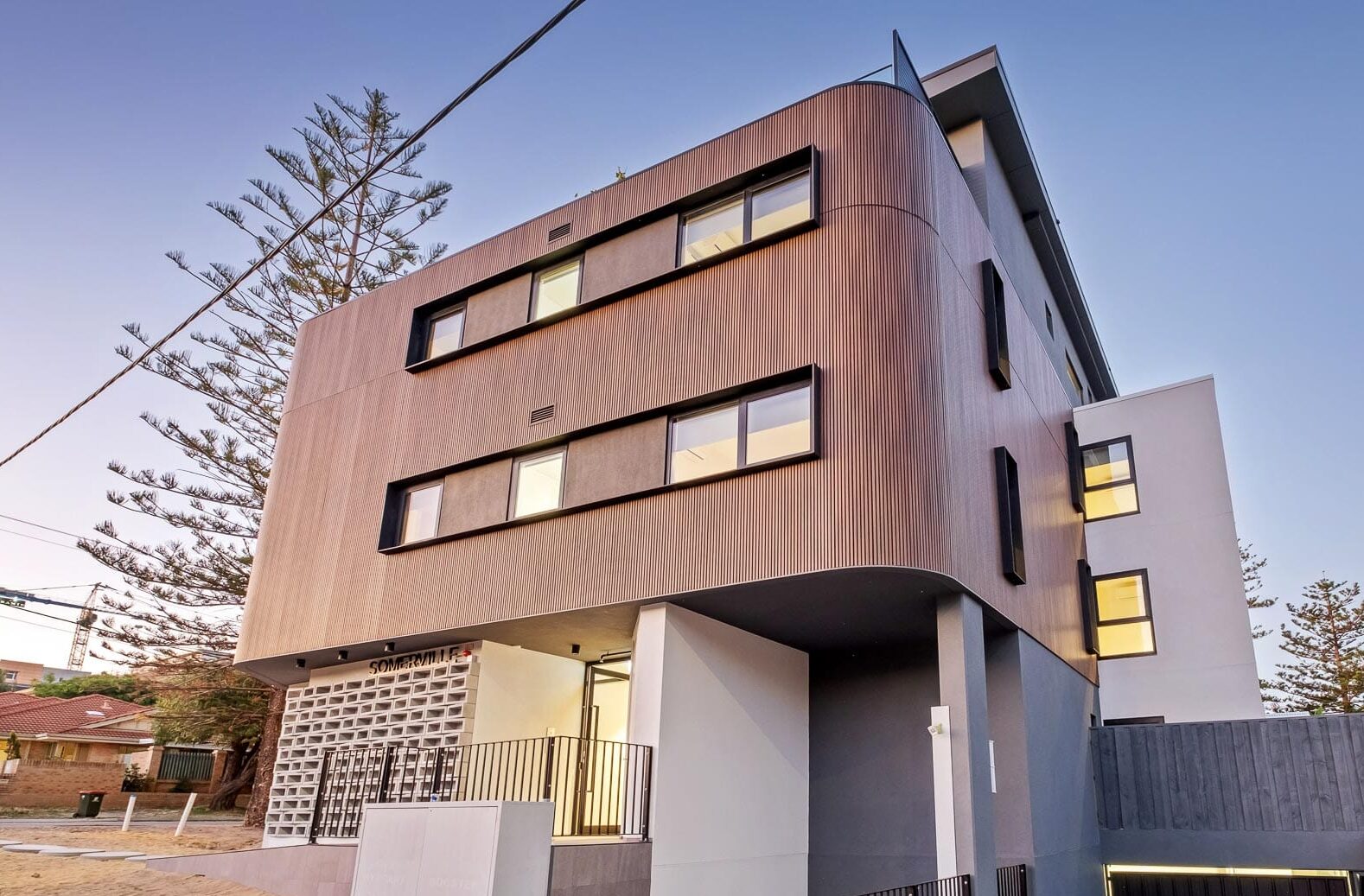 A modern residential building with curved wood cladding, large windows, and a mix of concrete and metal design elements.