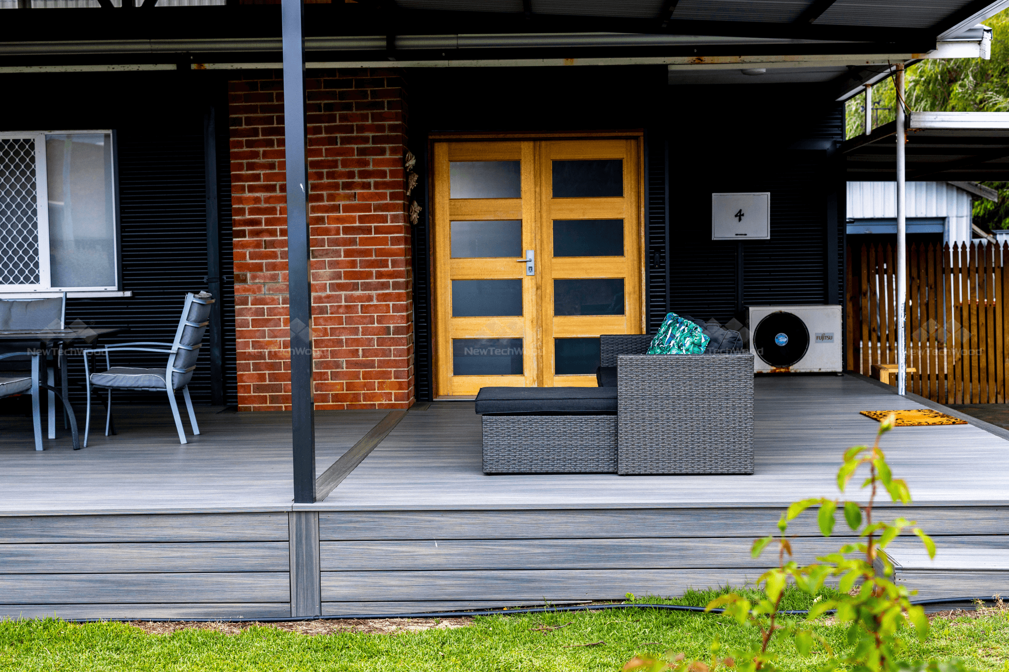 A stylish outdoor patio with grey composite decking, black furniture, and a modern wooden front door.