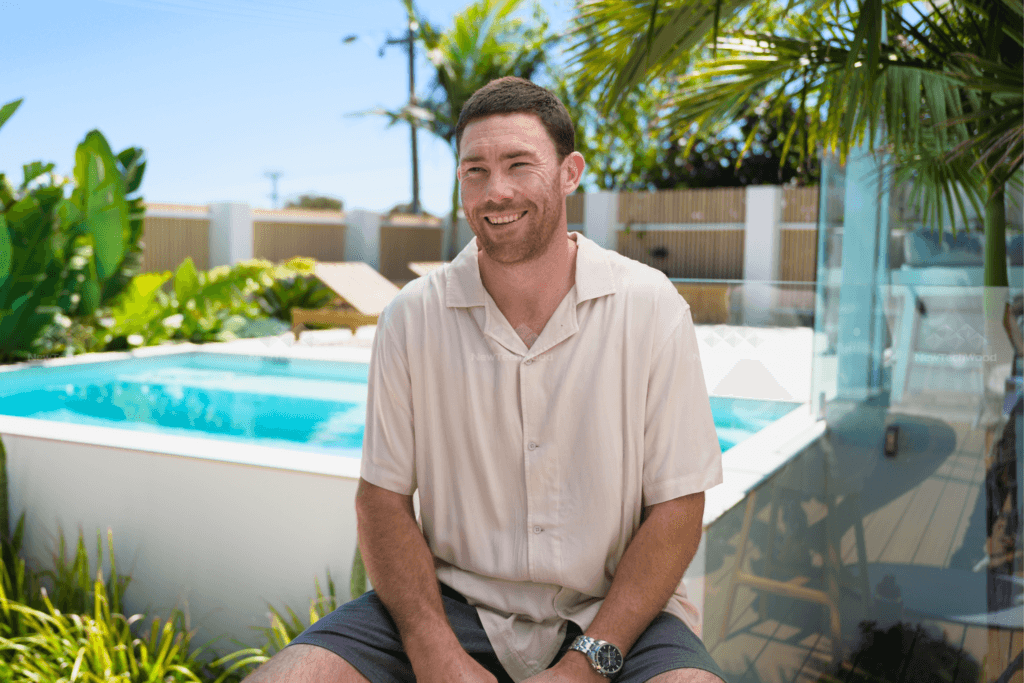 Jeremy McGovern sitting by the pool at his home, surrounded by lush greenery and modern outdoor decor.