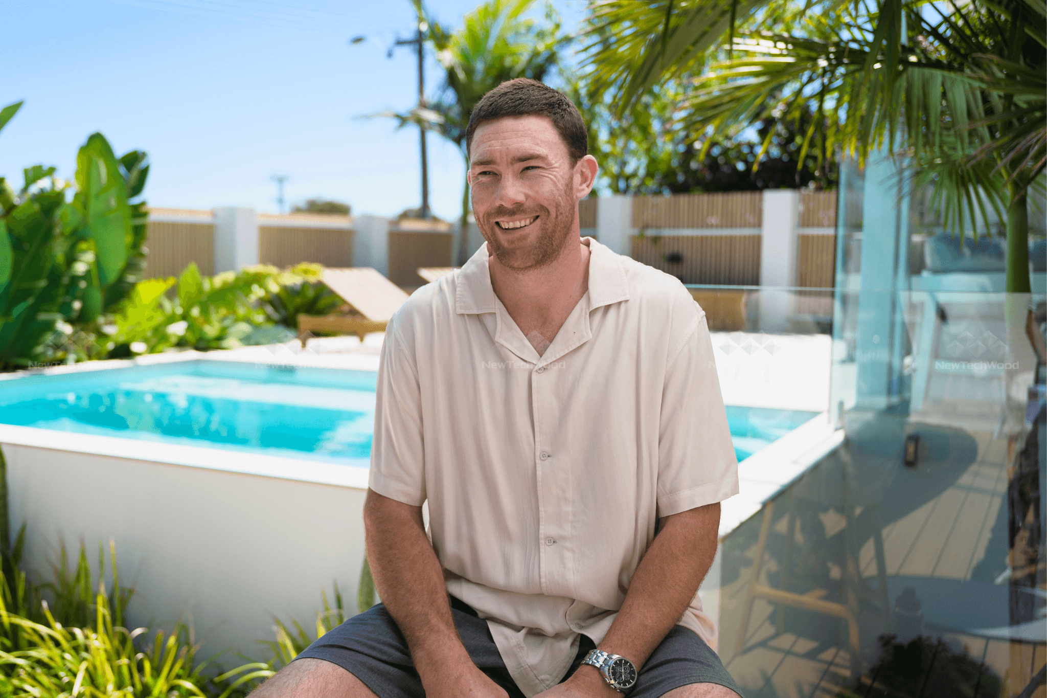 Jeremy McGovern sitting by the pool at his home, surrounded by lush greenery and modern outdoor decor.